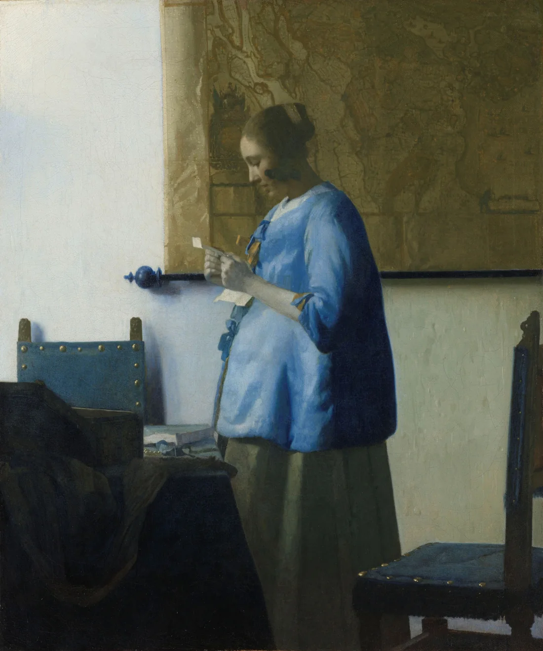 Vermeer’s Woman in Blue Reading a Letter: a young woman in a blue jacket stands in soft light reading a letter, a map on the wall behind her.